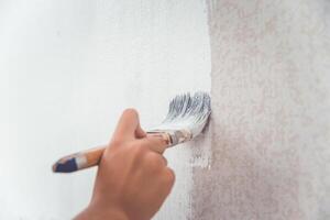 hand was holding a brush to paint the wall using white paint. photo