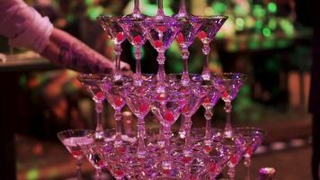 Glasses with Martini cocktail with ultraviolet color illumination. Clip. Champagne slide. Pyramid or fountain made of champagne glasses with cherry and steam from dry ice. empty glasses of martini in video