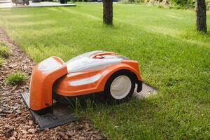 An orange robotic lawn mower stands on the base and is charged from electricity in the courtyard photo