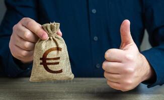 Thumbs up and euro money bag. The man approves the deal or loan. Agreement to be hired for a job at the offered salary. Profit-generating deposits savings. photo
