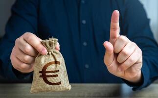 A man warns with his finger offering a euro money bag. Bad credit history. Funding and grants. Banks and finance. Terms of borrowing money. Strict conditions. Loan for a specific purpose. photo