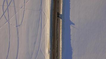 Aerial view over snowy field and road. The car on the road in the tundra, top view video