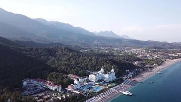 video. aereo Visualizza di Hotel su mare riva e montagne coperto con verde foresta, alberi con blu cielo a Alba. video. aereo Visualizza su riva del mare con lusso Hotel con foresta e montagne sfondo video