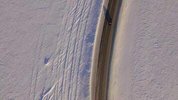 Suv rides on road through the snowy field. Aerial view on a snowy field and road from quadrocopter. Aerial view of snowy fields and road video