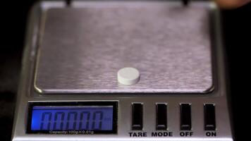 Close up of electronic scales being in use. Laboratory scales. Laboratory worker weighs the manufactured tablets on the control scales. Pills and medication health, close up video