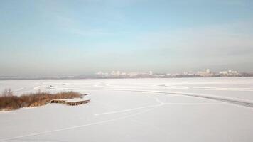 Cars ride by curvy ice track on snowy lake at winter evening during sunset. Aerial view. One car driving through the winter forest on country road. Top view from drone. video