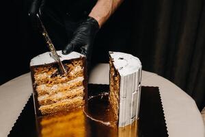 Amazing Cakes. A black-gloved chef is slicing a chocolate wedding cake. The wedding Cake is delicious inside on a black background.Large cake in white chocolate. photo