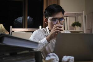 Young businessman working overtime on a desk at night. photo