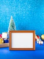 Christmas background with wooden frame mockup, blue glittering wall, and ornaments on blue navy desktop. photo