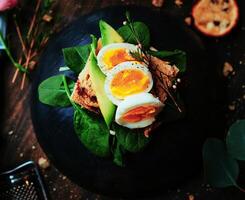 avocado toast with boiled eggs on a round black board and tea and cookies photo
