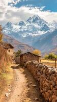 ai generado tranquilo campo escena presentando estrecho suciedad camino antiguo Roca y madera estructuras, con el majestuoso nieve tapado montañas en el fondo debajo parcialmente nublado cielo. ai generado foto