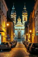 ai generado imagen de hermosamente iluminado barroco estilo iglesia, anidado Entre clásico arquitectónico edificios en guijarro calle a noche ai generado foto