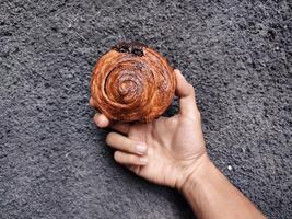 Hand holding Cromboloni, Round Croissant, New York Roll, a viral pastry combining croissants and bomboloni on concrete wall background. photo