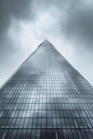 AI generated image shows tall skyscraper reaching into an overcast sky. The building is constructed with reflective glass panels that mirror the surrounding buildings and sky Ai Generated photo