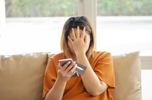 Stressed woman holding her face, scammer stealing money from online transaction, holding credit card and mobile phone photo