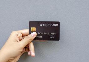 female hand holding a black credit card mockup with security chip embedded on a gray background photo