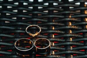 dos Boda anillos y uno compromiso anillo en un a cuadros red. Tres oro anillos de un Pareja en amor en un gris concepto de fondo de amor.boda anillo foto
