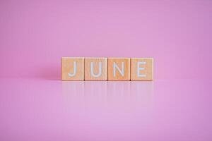 Wooden blocks form the text JUNE against a pink background. photo