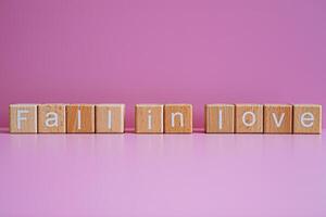 Wooden blocks form the text Fall in love against a pink background. photo