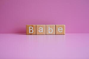 Wooden blocks form the text Babe against a pink background. photo