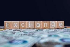 Wooden blocks with the text Exchange on a black background and crypto banknotes scattered on the ground. photo