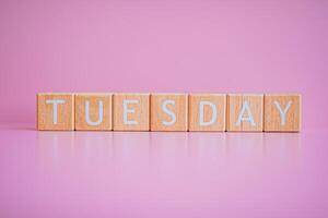Wooden blocks form the text TUESDAY against a pink background. photo