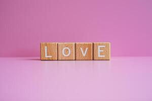 Wooden blocks form the text Love against a pink background. photo