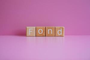 Wooden blocks form the text Fond against a pink background. photo