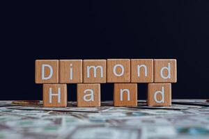 Wooden blocks with the text Dimond Hand on a black background and crypto banknotes scattered on the ground. photo