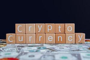 Wooden blocks with the text Cryptocurrency on a black background and crypto banknotes scattered on the ground. photo