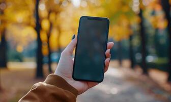 AI generated Female hand holding a smartphone with a blank screen in the autumn park photo