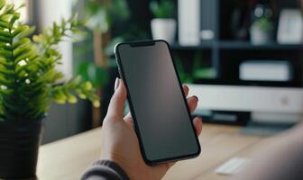 AI generated Mockup image of a woman's hand holding black mobile phone with blank screen on the table in modern office photo