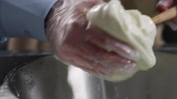 Dough stretching. Scene. Stretching a dough between two hands in metal bowl with water, dark background. Kneading dough with fingers video