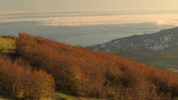 magnifique vue de petit bord de mer ville de le Haut de le Montagne couvert par des buissons sur bleu nuageux ciel Contexte. tir. aérien pour l'automne paysage de une côtier ville dans une ensoleillé journée de haute colline. video