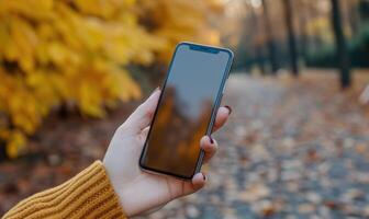 ai generado hembra mano participación un teléfono inteligente con un blanco pantalla en el antecedentes de el otoño parque foto