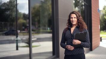 attraente attività commerciale donna con perdere lungo capelli a piedi Il prossimo per un ufficio edificio all'aperto con documenti nel mani video