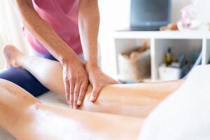 Crop female masseuse doing massage to leg of client in clinic photo