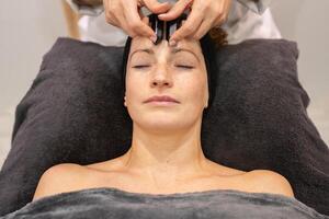 Professional beautician massaging face of woman with crystals photo