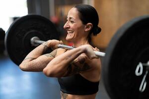 sonriente mujer levantamiento pesos en un cruzar formación gimnasio foto