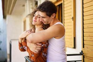 Loving couple engaged in romantic back hug on veranda of apartment photo