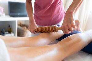 Crop masseuse doing physiotherapy massage with wooden device on client photo
