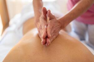 Crop osteopath massaging back with hands in salon photo