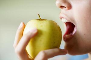 Crop teenage girl with mouth open eating yellow apple at home photo