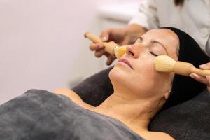 Crop beautician massage with brushes on female face in beauty salon photo