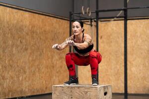 tatuado mujer hacer ejercicio utilizando caja en un cruzar formación gimnasio foto