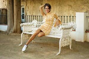 Stylish happy young woman sitting on iron bench outdoors photo