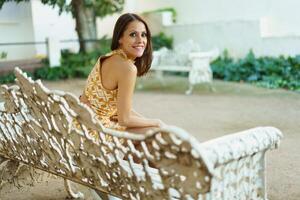 Positive young woman smiling while sitting on bench in park photo