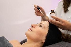 Crop beautician putting serum on client face in beauty salon photo
