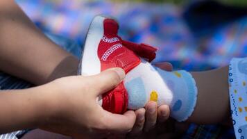 de la madre manos son poniendo en bebé caminando rojo zapatillas para su niñito hijo con amor y cuidado. niño pone en Zapatos y medias. foto