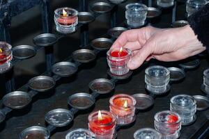 oración velas dentro un católico iglesia. un mujer mano sostiene un vela. foto